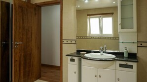 Un baño con una puerta de madera, un lavabo con un espejo encima y una ventana sobre el espejo.