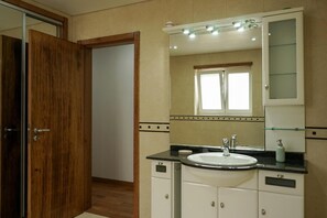 A bathroom with a wooden door, a sink with a mirror above it, and a window above the mirror.