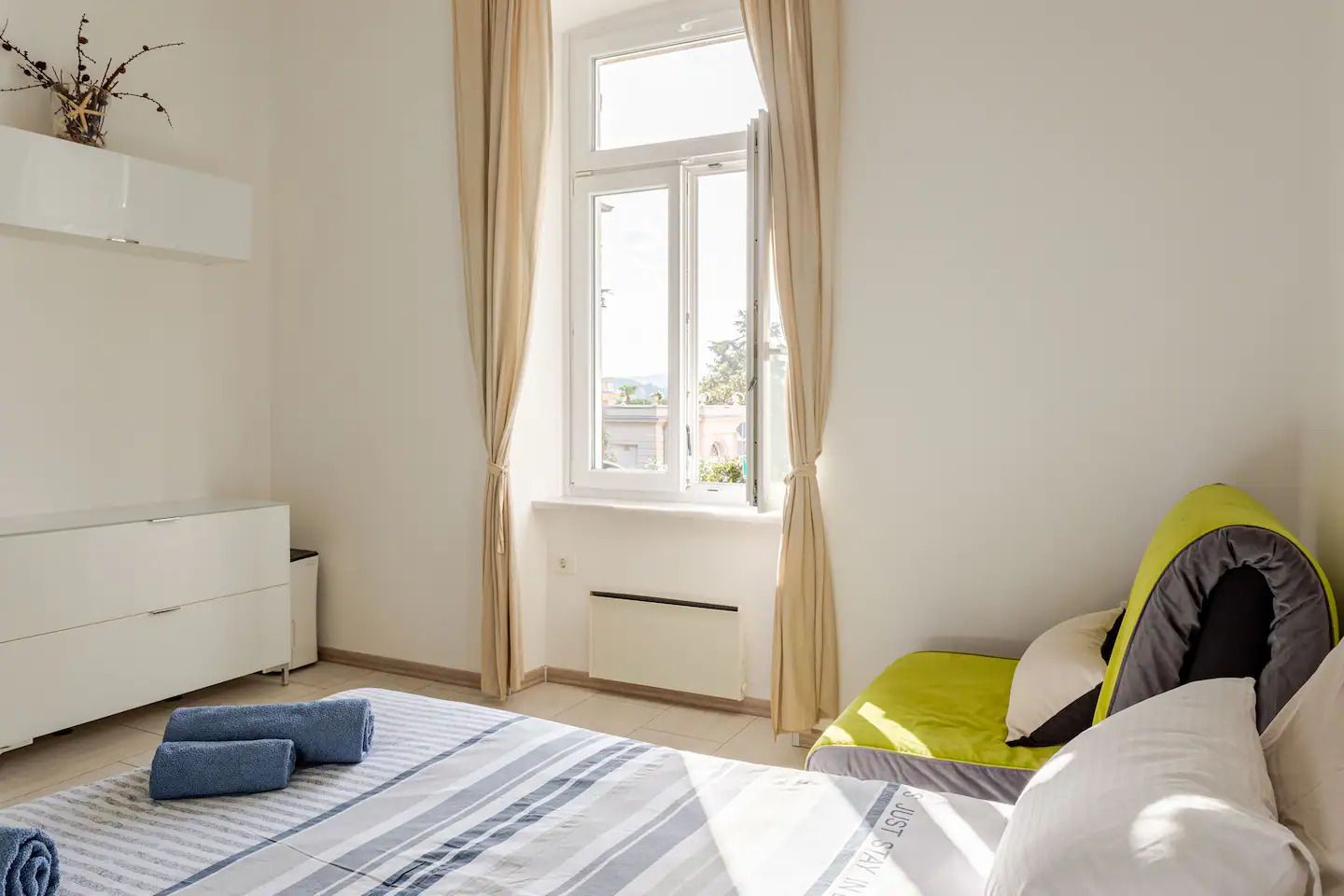 A bedroom with a bed, a bedside table, a window with curtains, and a view of the outside.