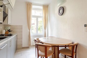 Eine Küche mit Esstisch und Stühlen, einem Fenster mit Vorhängen sowie einer Wandleuchte.
