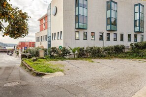Ein modernes Gebäude mit großen Fenstern, einer Schotterfläche davor und einer Straße mit Fahrzeugen.