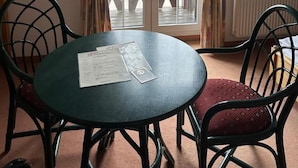 A room with a round table and two chairs, a window with curtains, and a view of a deck outside. - Hotel Am Spreebogen (Burg (Spreewald))