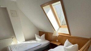 A bedroom with two beds, a wooden headboard, a nightstand, a lamp, and a window. - Hotel Am Spreebogen (Burg (Spreewald))