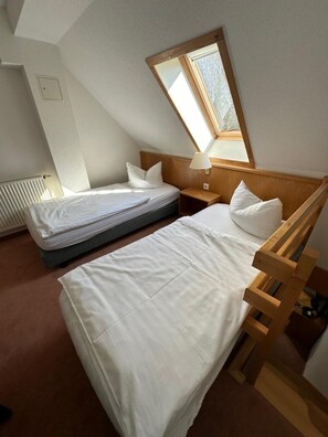 A bedroom with two beds, a wooden headboard, a nightstand, a lamp, and a window. - Hotel Am Spreebogen (Burg (Spreewald))