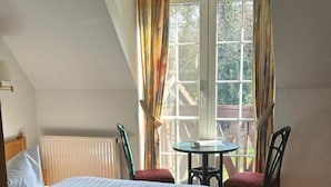 A bedroom with a bed, a table, two chairs, and a window with curtains. - Hotel Am Spreebogen (Burg (Spreewald))