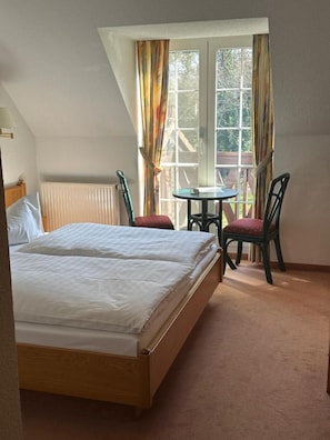 A bedroom with a bed, a table, two chairs, and a window with curtains. - Hotel Am Spreebogen (Burg (Spreewald))