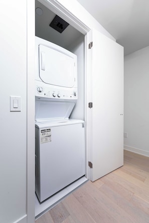 Ett kompakt, vitt tvättrum med en inbyggd tvättmaskin och torktumlare, en tydlig energimärkning och en ljusströmbrytare på väggen.