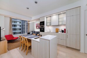 Una cocina moderna con una isla central, una zona de comedor con una silla roja y un ventanal con cortinas.