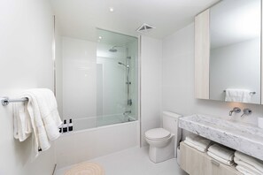 Ein modernes Badezimmer mit einer gläsernen Duschkabine, einer Toilette und einer Marmorwaschtischplatte mit Waschbecken.