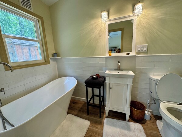 A bathroom with a freestanding bathtub, a sink, a toilet, and a mirror above the sink.