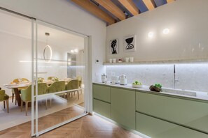 A modern kitchen with green cabinets, a dining area with green chairs, and a glass partition. - Apartment in Lucca Near Iconic Landmarks (Lucca)