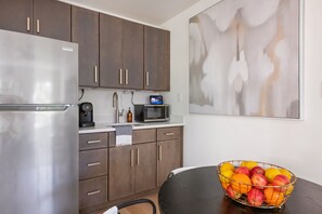 A modern kitchen with a refrigerator, microwave, coffee maker, and a fruit bowl on the counter. - Beltline Bungalow (Atlanta)
