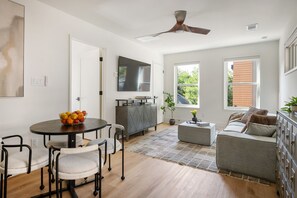 A modern living room with a dining area, a grey sofa, a TV, and a ceiling fan. - Beltline Bungalow (Atlanta)
