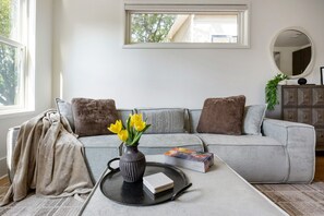 A modern living room with a grey sofa, a round coffee table, and a vase with yellow flowers. - Beltline Bungalow (Atlanta)