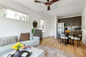 A modern living room with a sofa, a coffee table, and a dining area with chairs and a kitchen in the background. - Beltline Bungalow (Atlanta)