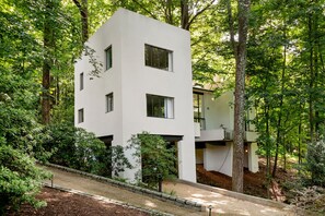 A modern two-story building with a white facade, surrounded by dense greenery and trees. - Crystal Claire (Atlanta)
