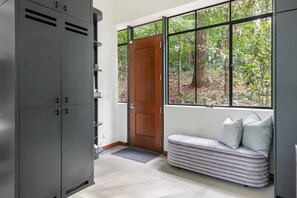 A room with a grey cabinet, a wooden door, a bench with cushions, and a window with a view of trees. - Crystal Claire (Atlanta)