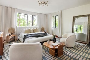 A hotel room with a large bed, two bedside tables, a chair, a mirror, and a view of trees through the windows. - Crystal Claire (Atlanta)