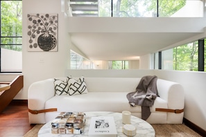 A modern living room with a white sofa, patterned cushions, a marble coffee table, and a large window with a view of trees. - Crystal Claire (Atlanta)