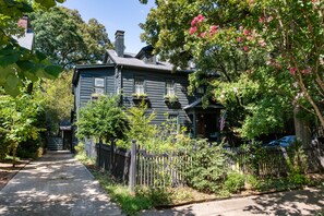 A two-story house with a dark exterior, a front porch with a railing, and a pathway leading to the entrance. - Atelier Bleu (Atlanta)