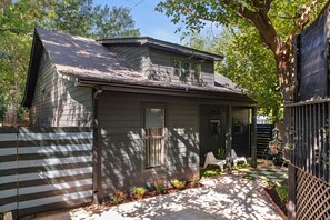 A two-story house with a dark siding exterior, a front porch with a bench, and a small garden area with flowers and shrubs. - Atelier Bleu (Atlanta)
