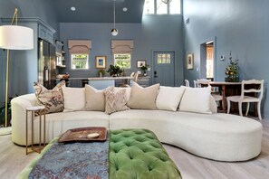 A modern living room with a sectional sofa, a green ottoman, and a dining area with a wooden table and chairs. - Atelier Bleu (Atlanta)