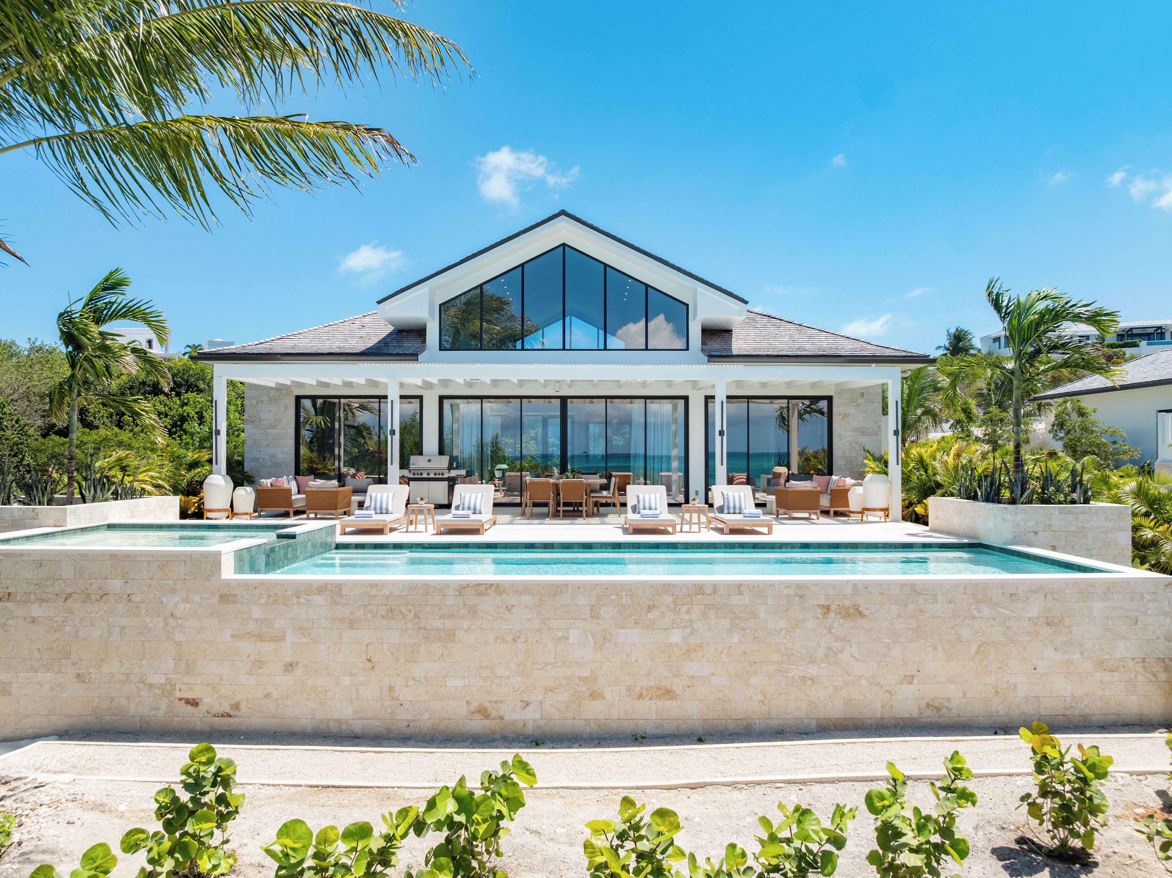 A modern two-story house with a swimming pool, outdoor seating area, and a view of the ocean.