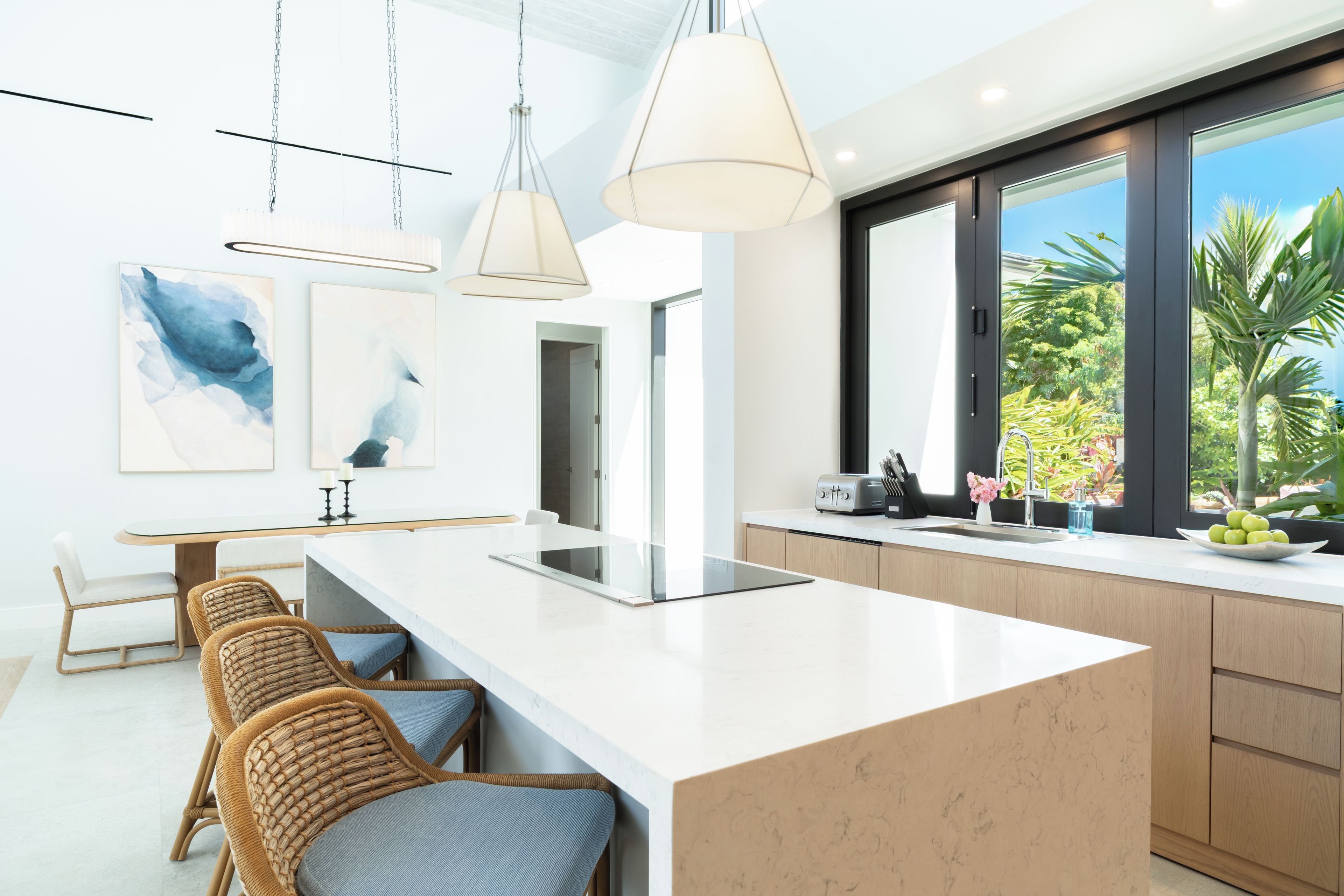 A modern kitchen with a central island, pendant lighting, and a view of greenery outside.