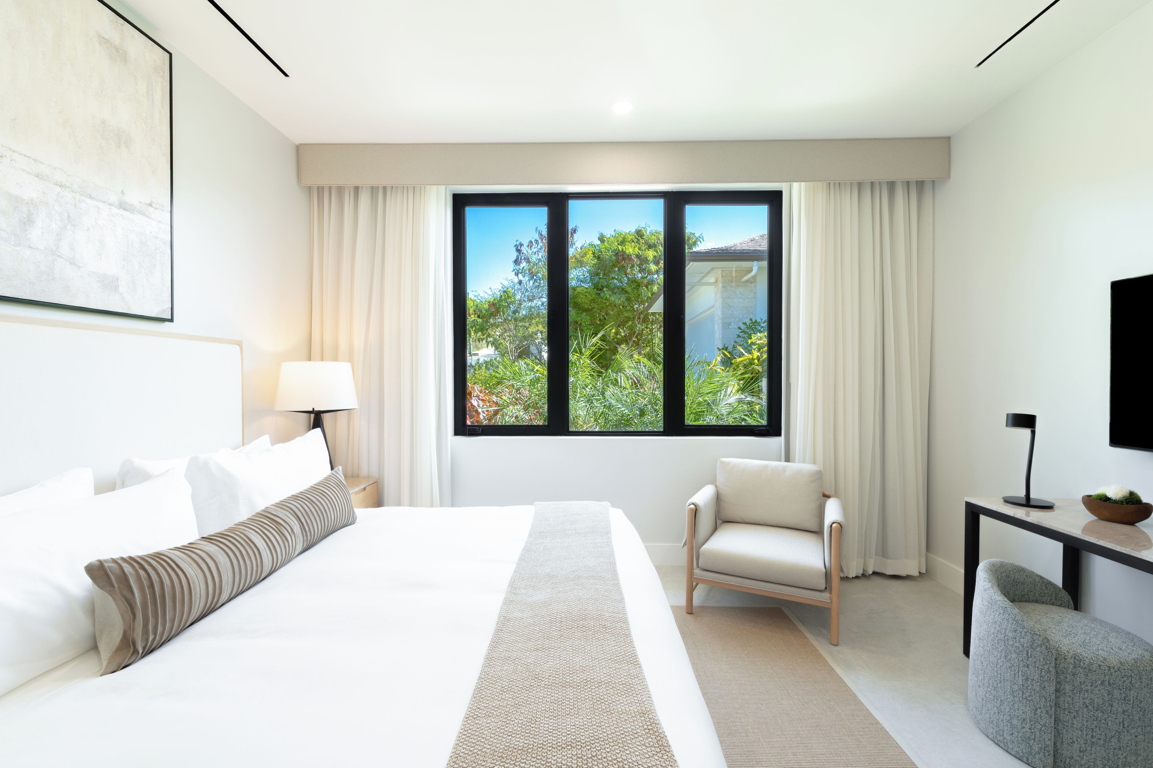 A modern hotel room with a large bed, a seating area, and a window with a view of greenery.