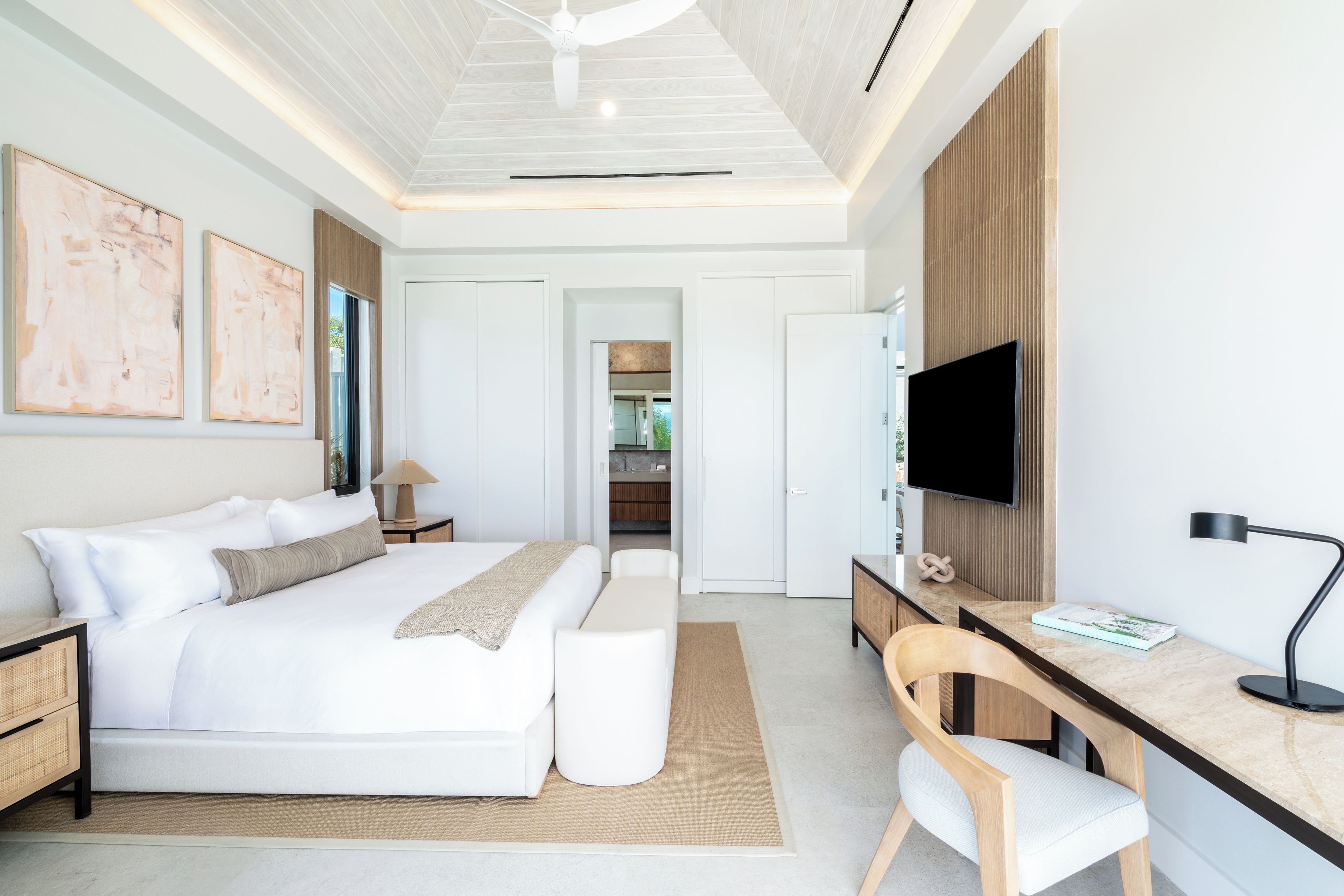 A modern bedroom with a large bed, a desk, and a television.