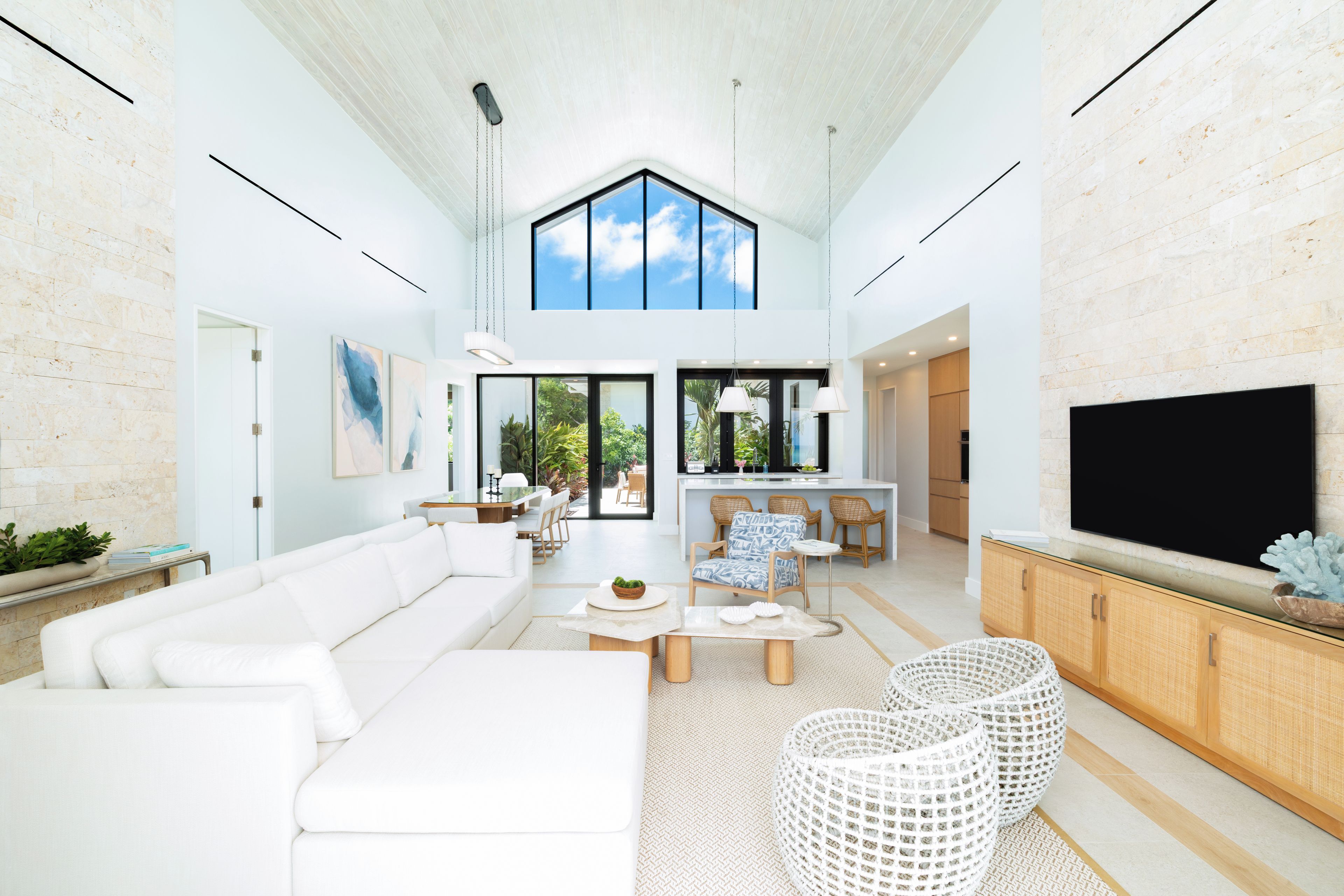 A spacious living area with a high ceiling, a large TV, and a dining area with wicker furniture.
