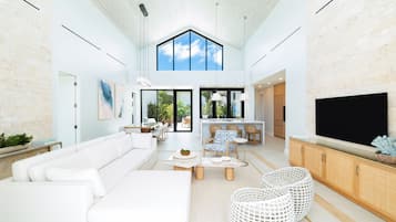 A spacious living area with a high ceiling, a large TV, and a dining area with wicker furniture.