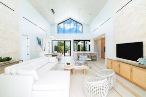 A spacious living area with a high ceiling, a large TV, and a dining area with wicker furniture.