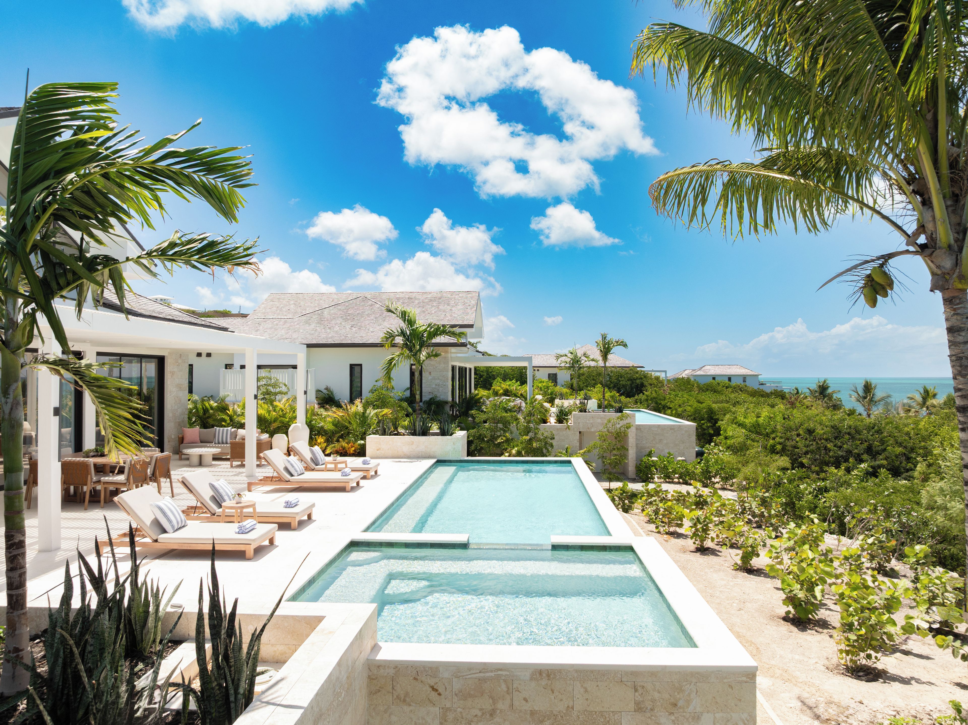 A modern poolside area with lounge chairs, a pool, and a view of the ocean.