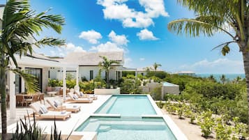 A modern poolside area with lounge chairs, a pool, and a view of the ocean.