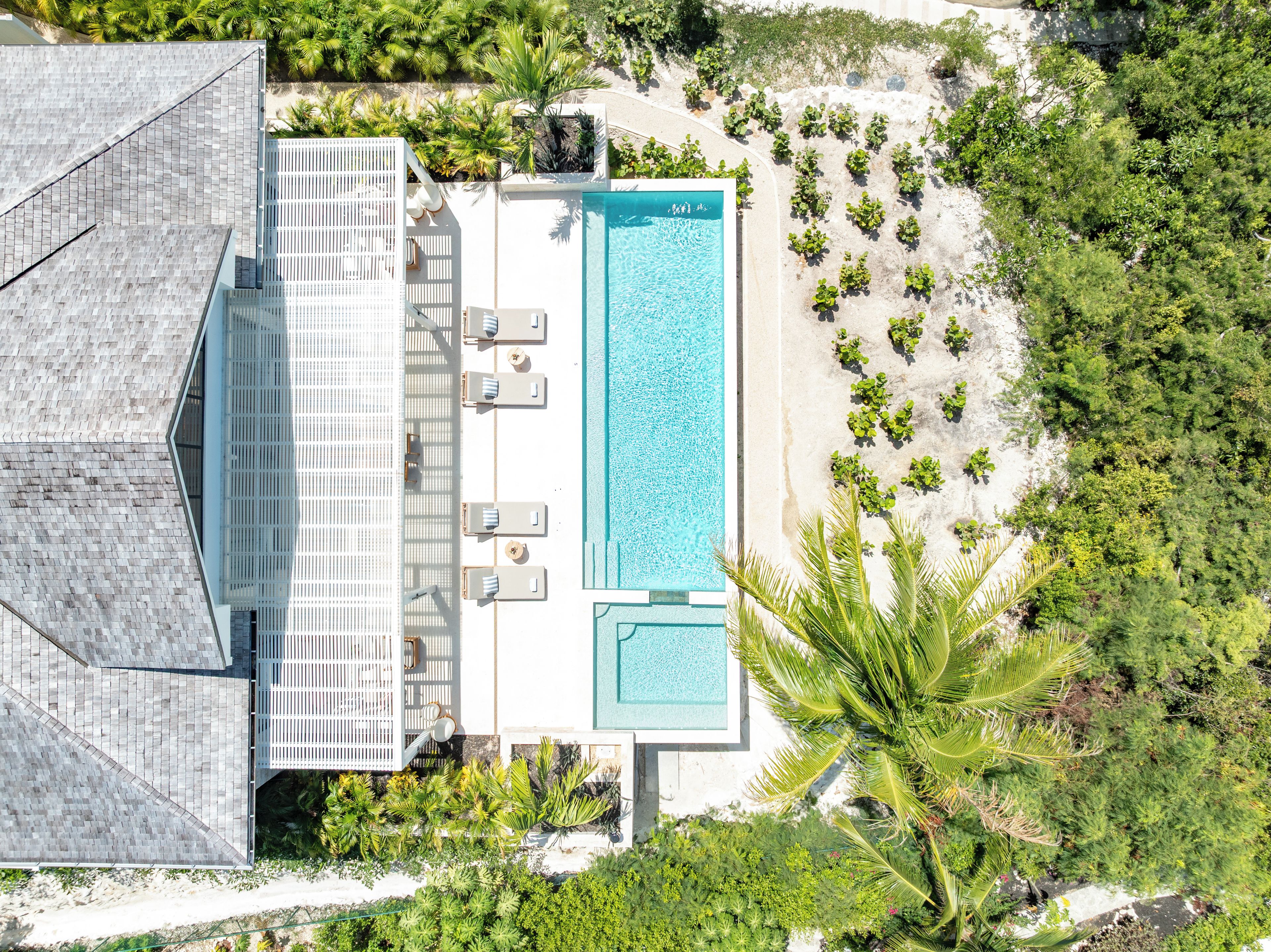 Luchtbeeld van een resort met een zwembad, ligbedden en een strandgedeelte.
