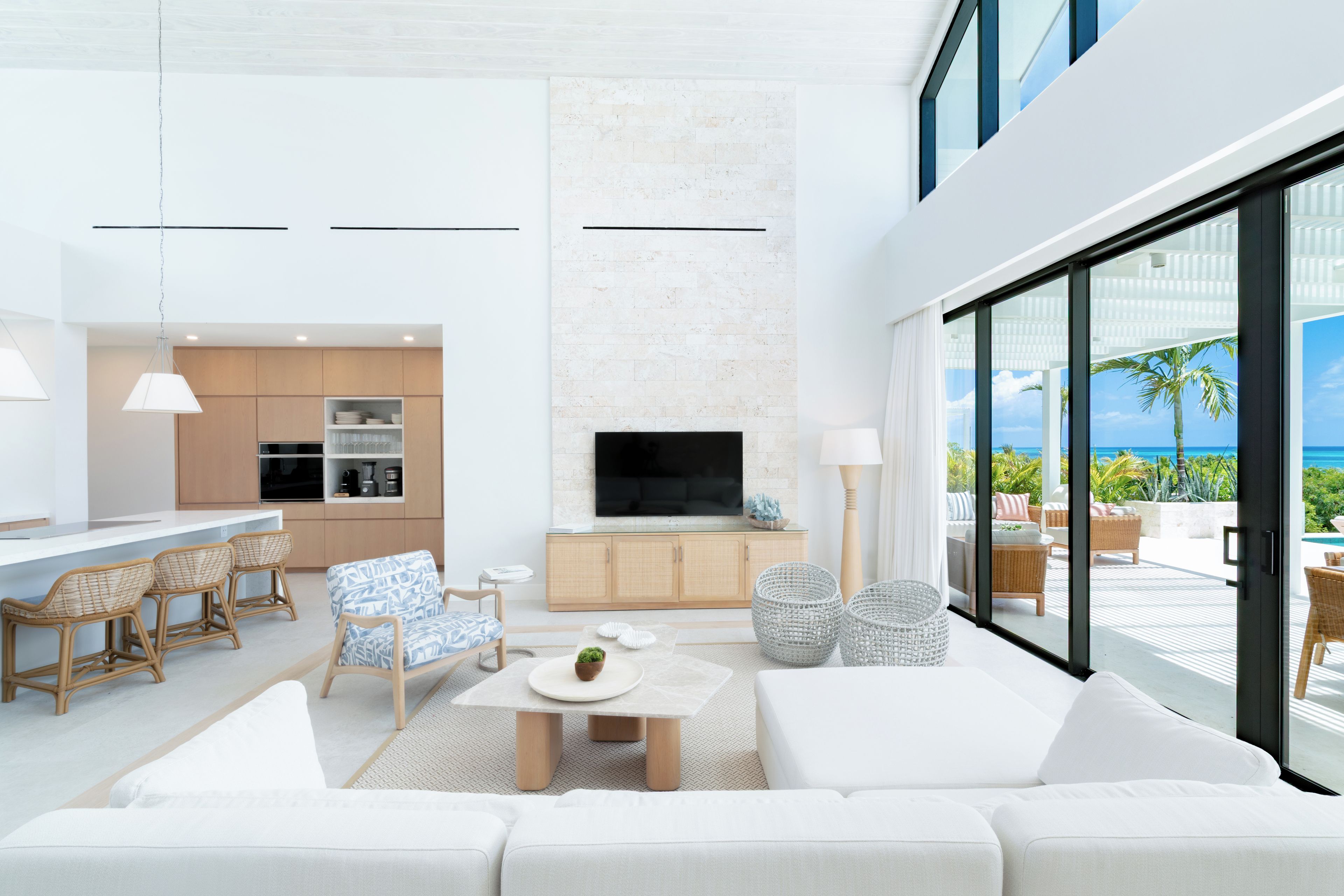Uma sala de estar moderna com um sofá grande, uma área de jantar com cadeiras, uma cozinha com armários e uma TV fixada na parede.