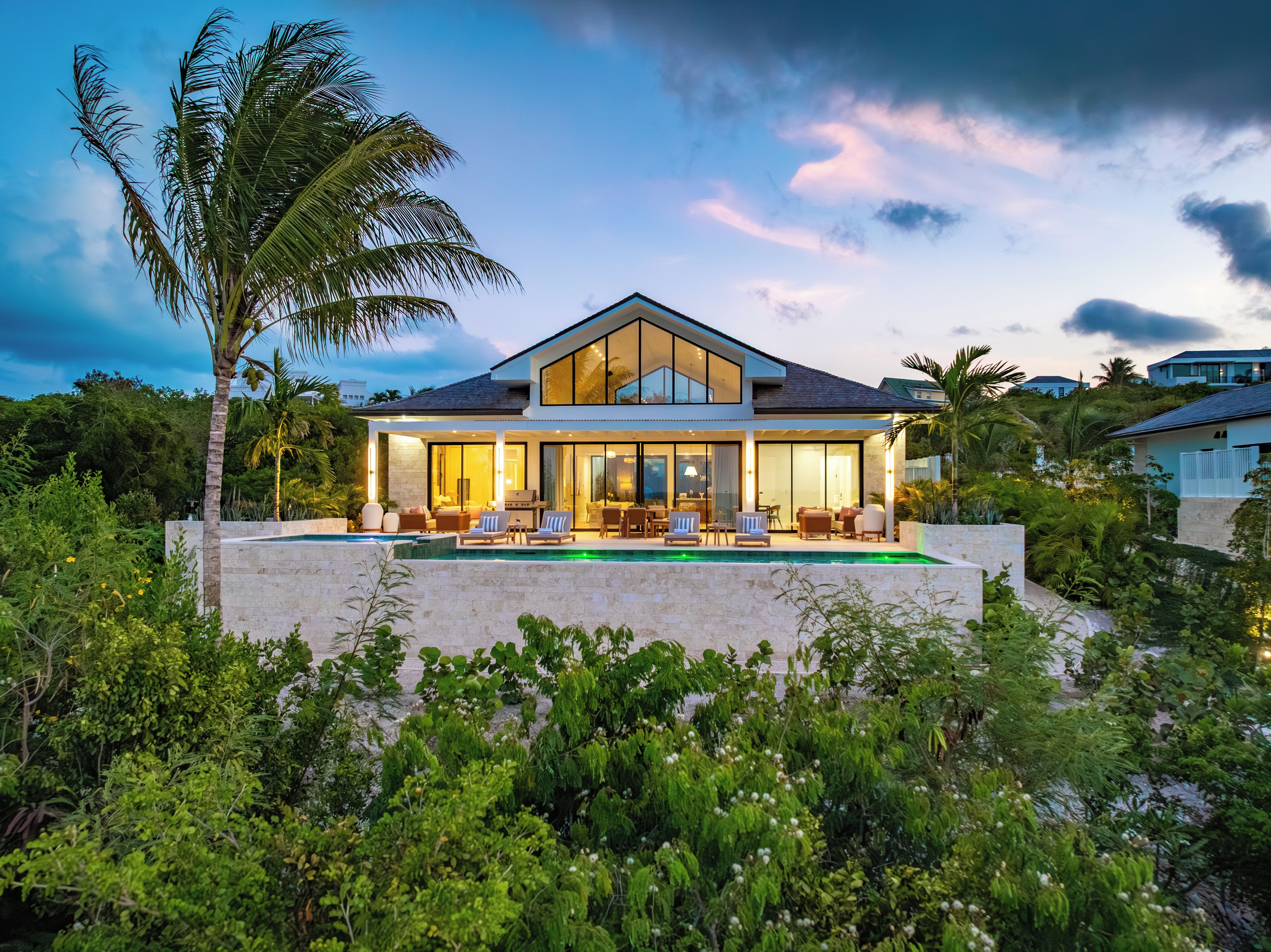 Une maison moderne avec une piscine, entourée d’une végétation luxuriante et de palmiers.