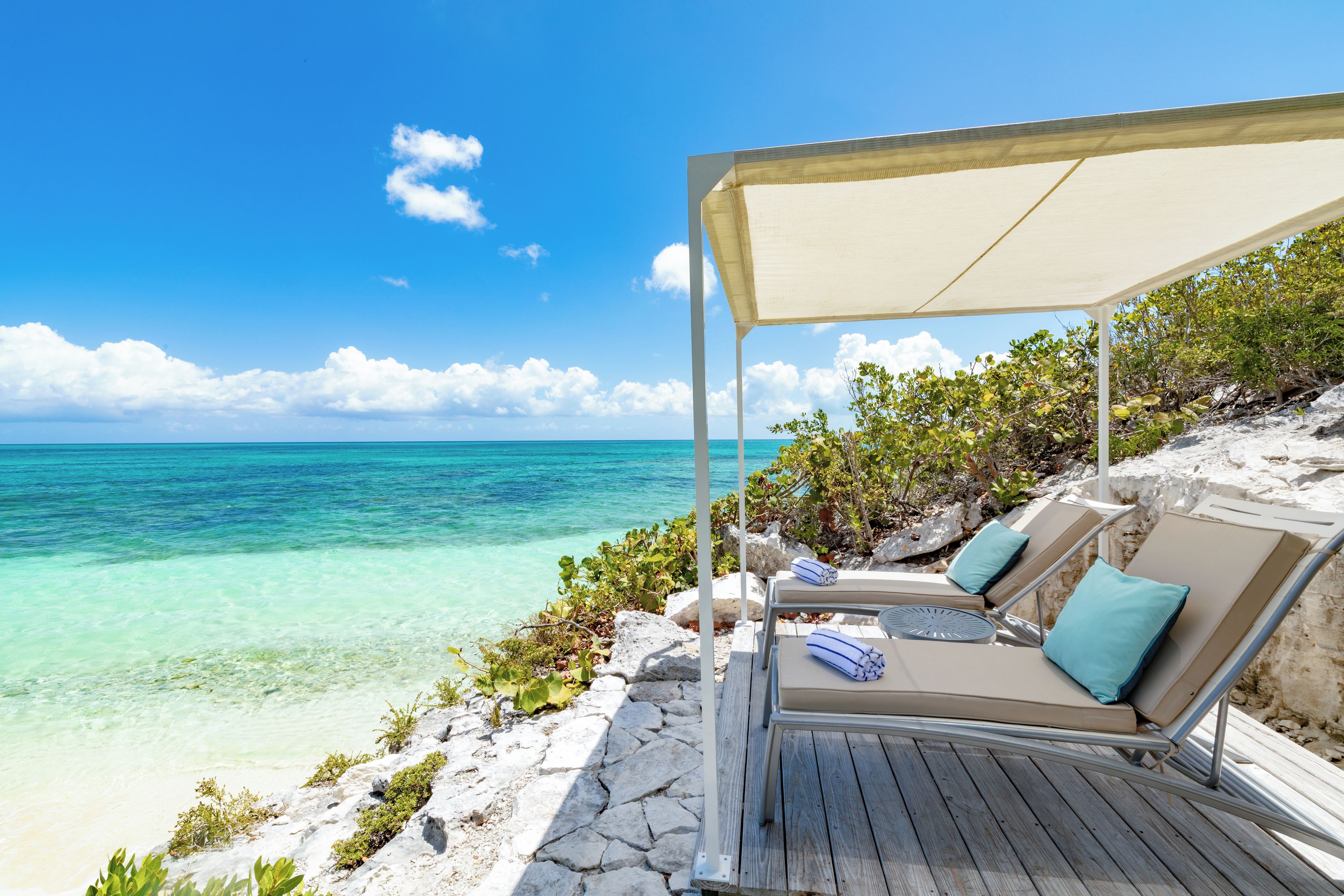 A beachside lounge with a canopy, two lounge chairs, and a view of the ocean.