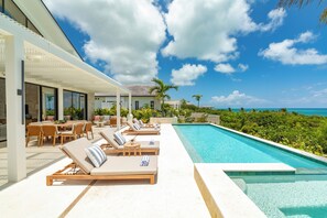 Un área junto a la piscina con sillones reclinables y una zona de comedor.