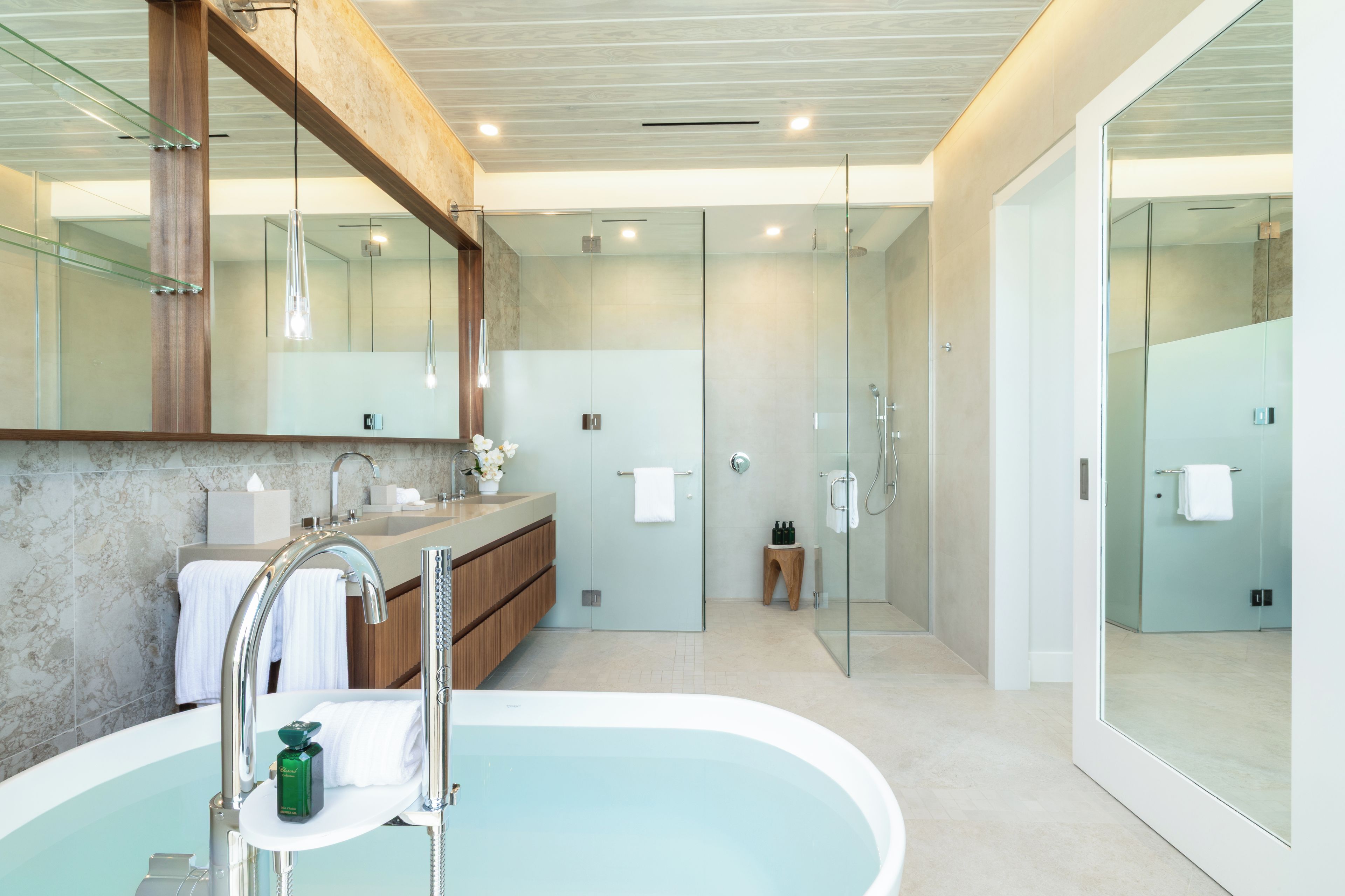 Een moderne badkamer met een vrijstaand bad, een douche met glazen wanden en een wastafel met een marmeren aanrecht.