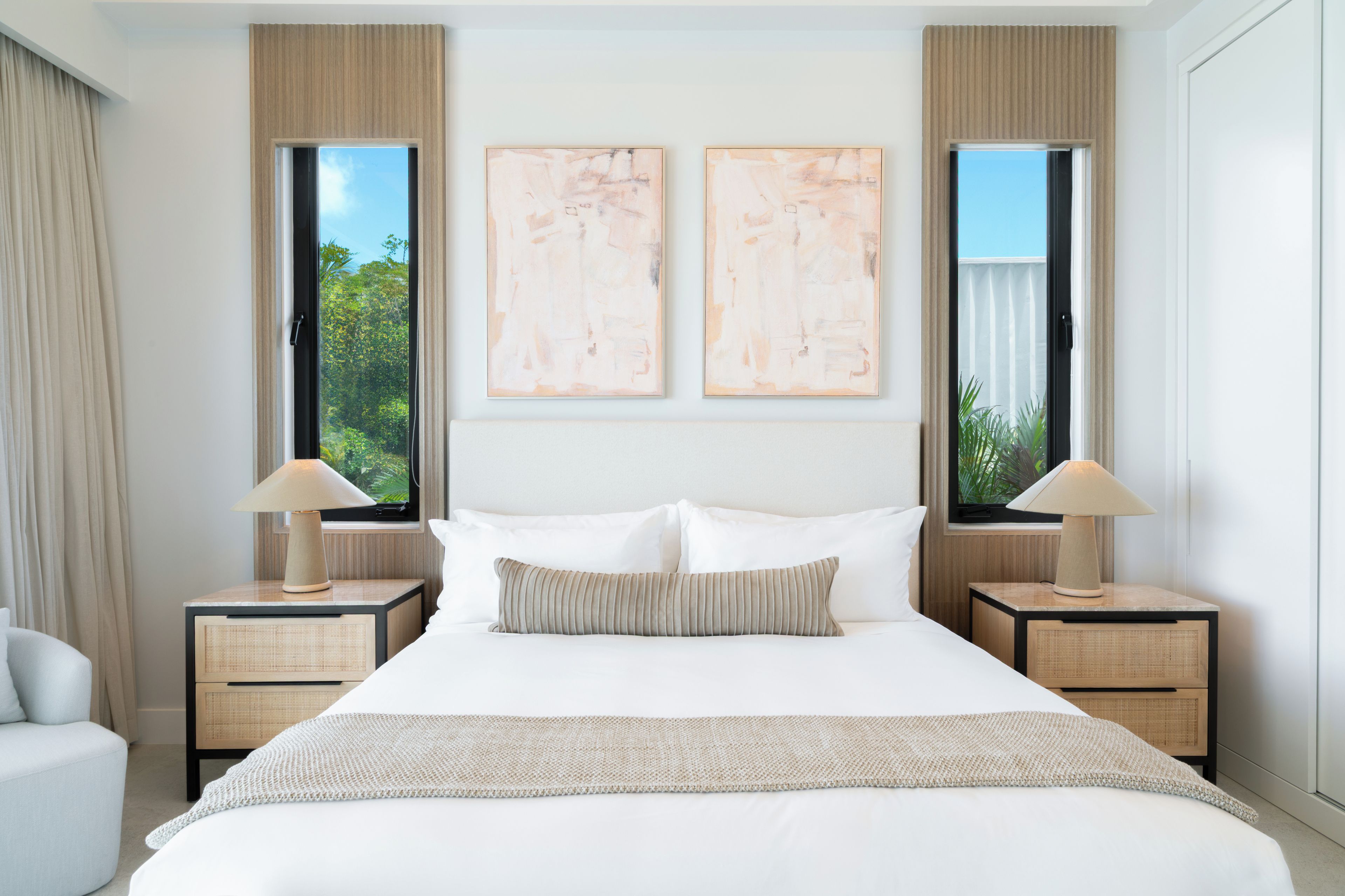 Une chambre d’hôtel avec un grand lit, deux tables de chevet, une fenêtre et deux tableaux abstraits accrochés au mur.