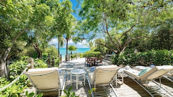 Une terrasse en bois, agrémentée de chaises longues et d’une table, entourée d’une végétation luxuriante et offrant une vue sur la plage.