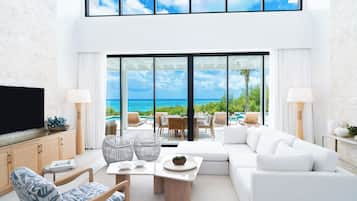 A modern living room with a large TV, comfortable seating, a dining area, and a view of the ocean.