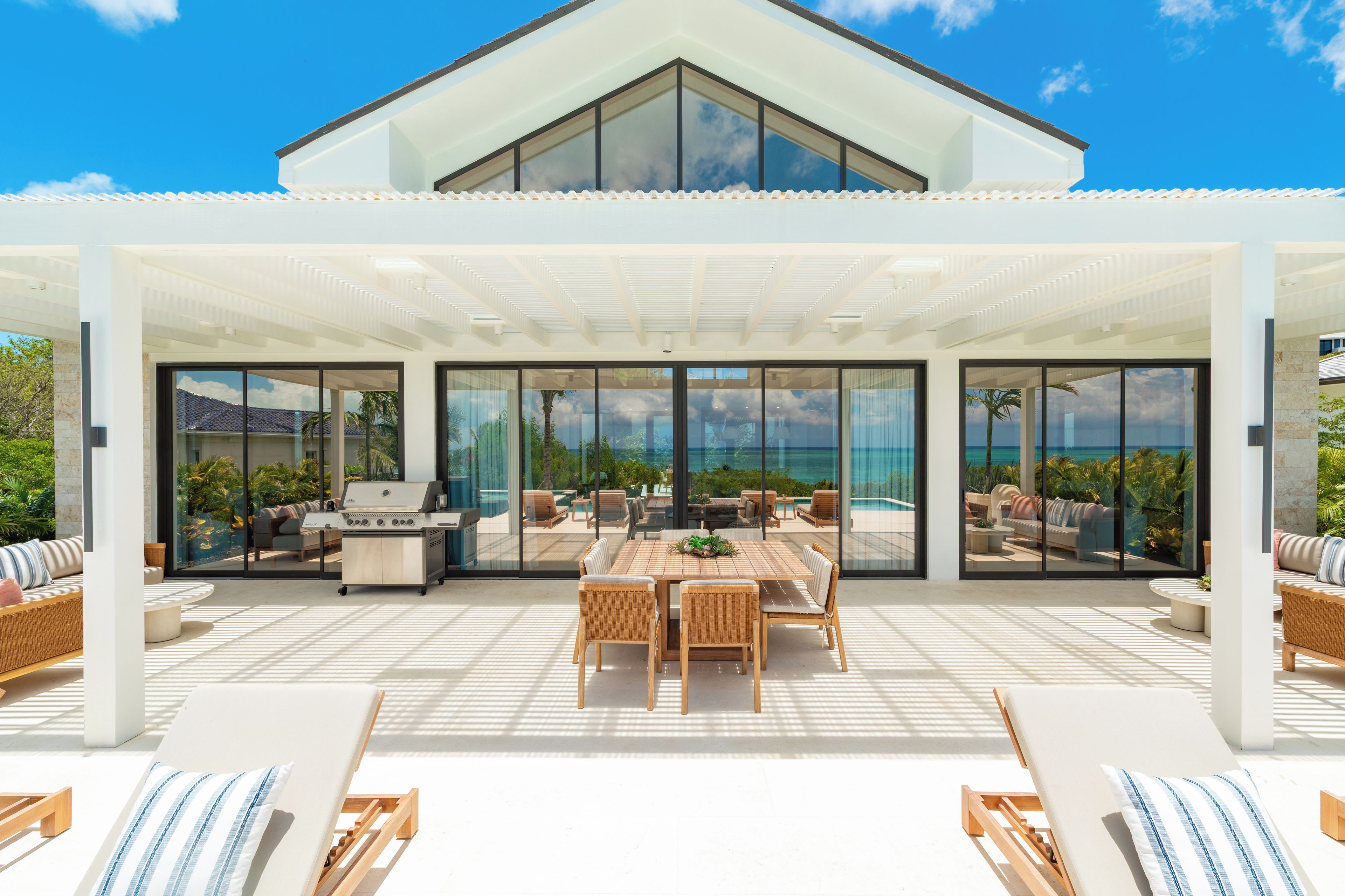 Une terrasse extérieure moderne comprenant un espace repas, des fauteuils de salon et un barbecue.