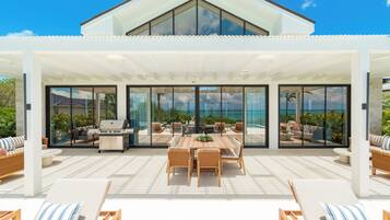 Une terrasse extérieure moderne comprenant un espace repas, des fauteuils de salon et un barbecue.