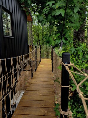 A wooden pathway leading to a black building with a window, surrounded by greenery and rope barriers.