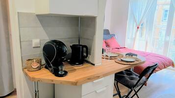 Eine kompakte Küche mit Kaffeemaschine, Mülleimer und kleinem Kühlschrank.
