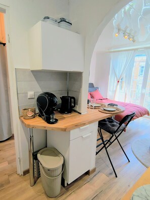 Eine kompakte Küche mit Kaffeemaschine, Mülleimer und kleinem Kühlschrank.