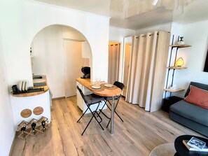 A compact living space with a dining area, a sofa, and a small table with a lamp. - Studio 'Centre Historique, 500m de la gare, quartier Steinbach' with Balcony (Mulhouse)
